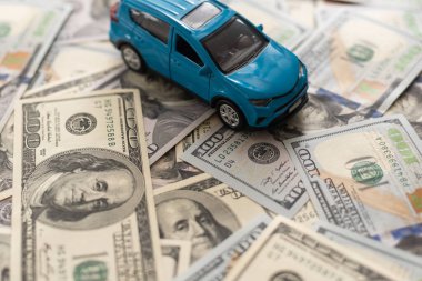 100 dolarlık banknotlarda küçük oyuncak araba, beyaz arka planda izole edilmiş yol olarak.