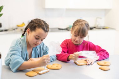 Evdeki mutfakta ev yapımı kurabiyeleri dekore eden iki kız kardeş..