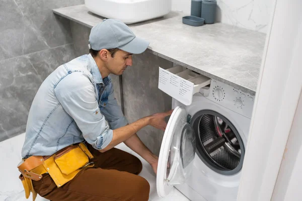 Homem trabalhador encanador repara uma máquina de lavar roupa na lavanderia — Fotografia de Stock