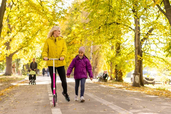 엄마가 공원에서 아기 스쿠터를 타고 딸과 함께 걸어 다닐 때. — 스톡 사진