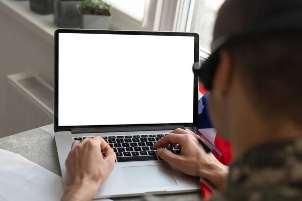 Militar gesto en la oficina cerca de la computadora portátil con pantalla en blanco, bandera de EE.UU.. — Foto de Stock