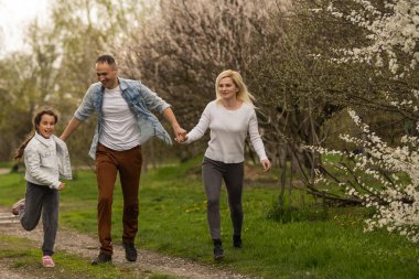Mutlu genç aile dışarıda yeşil doğada birlikte vakit geçiriyor.