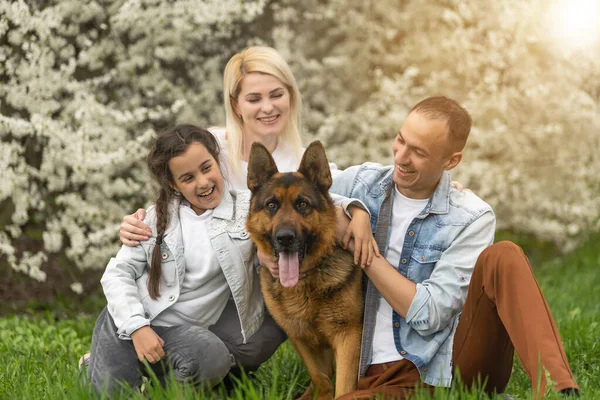 Familia feliz al aire libre pasando tiempo juntos. Padre, madre e hija se están divirtiendo en una hierba floral verde . — Foto de Stock