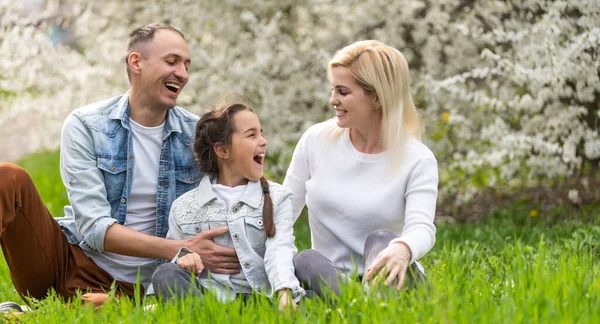 Mutlu bir aile açık havada birlikte vakit. Baba, anne ve kızı bir yeşil çiçek çimenlerin üzerinde eğleniyor musun.