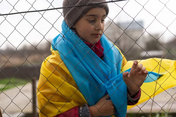 Metal bir çitin arkasında üzgün üzgün bakan küçük bir mülteci kız. Mültecilerin ve yerlerinden edilen insanların sosyal sorunları. Rusya 'nın Ukrayna halkına karşı savaşı