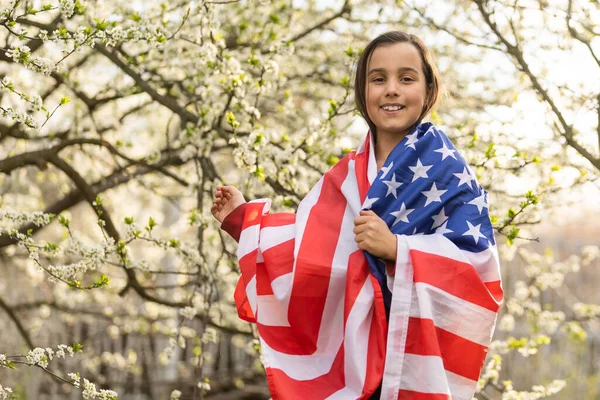Gülümseyen ve Amerikan bayrağı sallayan sevimli küçük kız. Vatansever bayram. Mutlu çocuk, Amerikan bayrağı taşıyan şirin küçük kız çocuğu. ABD 4 Temmuz 'u kutluyor. Bağımsızlık Günü kavramı.