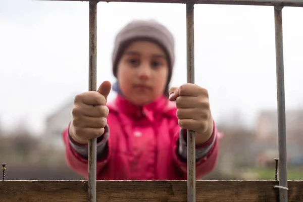 Klein meisje achter de tralies. Begrip dakloze kinderen. Kindergevangenschap. Droevig kind — Stockfoto