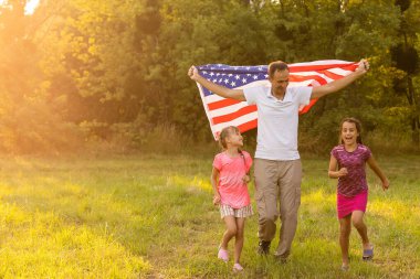 Vatansever bayram. Mutlu aile, gün batımında Amerikan bayrağı taşıyan anne ve kızları. ABD 4 Temmuz 'da bağımsızlığını kutladı.