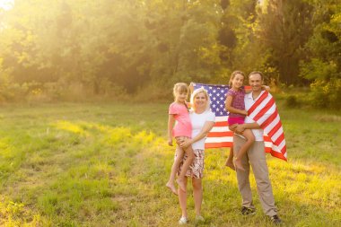Vatansever bayram. Mutlu aile, gün batımında Amerikan bayrağı taşıyan anne ve kızları. ABD 4 Temmuz 'da bağımsızlığını kutladı.