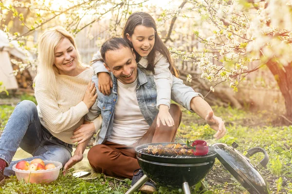 Família feliz fazendo um churrasco em seu jardim na primavera. Conceito de lazer, alimentação, família e feriados. — Fotografia de Stock