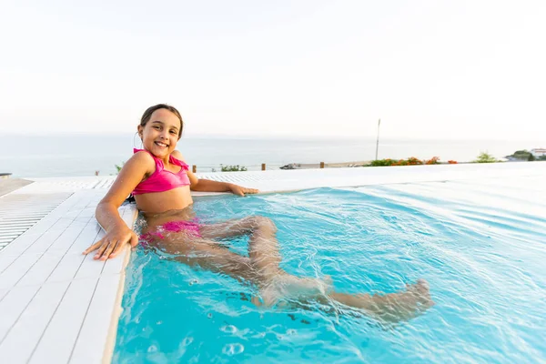 Niña jugando en la piscina al aire libre saltando al agua en las vacaciones de verano en la isla de playa tropical. Niño aprendiendo a nadar en la piscina al aire libre del complejo de lujo . —  Fotos de Stock
