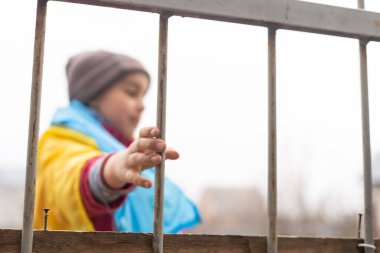 Metal bir çitin arkasında üzgün üzgün bakan küçük bir mülteci kız. Mültecilerin ve yerlerinden edilen insanların sosyal sorunları. Rusya 'nın Ukrayna halkına karşı savaşı
