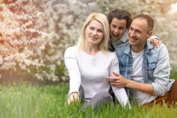 Retrato ao ar livre de família jovem feliz jogando no parque da primavera sob a árvore florescente, linda família se divertindo no jardim ensolarado — Fotografia de Stock