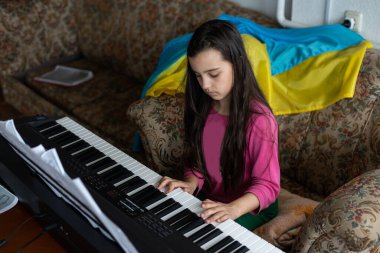 Portrait of rescued little girl playing synthesizer with flag of ukraine