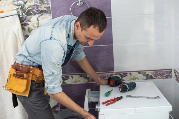 working man plumber repairs a washing machine in laundry