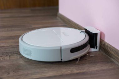 Kabartma ahşap zemin üzerindeki robot elektrikli süpürge ana istasyondan şarj oluyor. Akıllı temizlik teknolojisi. Robot elektrik süpürgesi temiz oda zeminindeki şarja geri döndü.