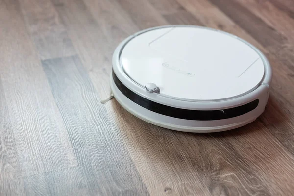 Kaplamalı ahşap zeminde beyaz bir elektrikli süpürge robotu. Oturma odasını temizleme fikri.
