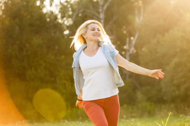 Çekici genç bir kadın, arka planda günbatımıyla parkta eğleniyor..