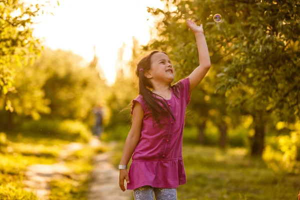 Fünfjähriges kaukasisches Mädchen pustet bei Sonnenuntergang Seifenblasen im Freien - glückliche unbeschwerte Kindheit. — Stockfoto
