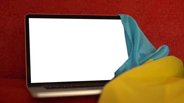 Laptop mit leerem Bildschirm auf dem Tisch und ukrainischer Nationalflagge im Hintergrund, Platz für Text. — Stockfoto