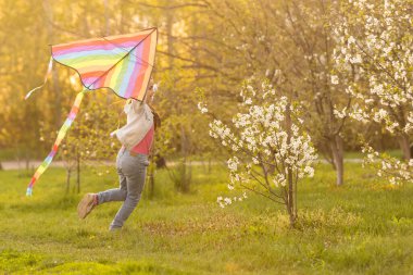 Uçurtması olan mutlu bir kız çocuğu doğada çayırlarda koşuyor..