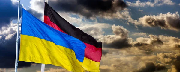 Ukraina i Niemcy machają flagami na błękitne i zachmurzone niebo. Stań z Ukrainą. — Zdjęcie stockowe