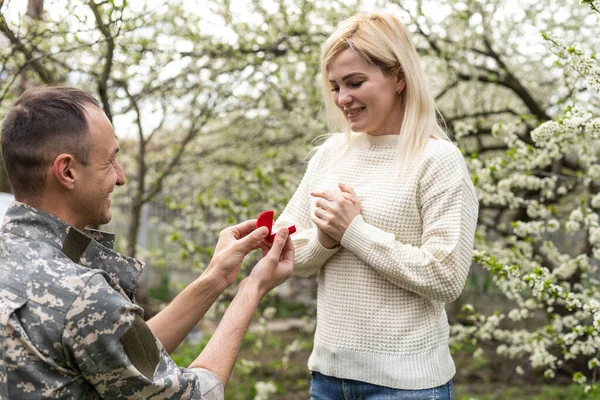 Soldier on his knees asking for marriage by holding the hands of his partner woman and giving an engagement ring. Concept patriotism, war, soldier. — Fotografia de Stock