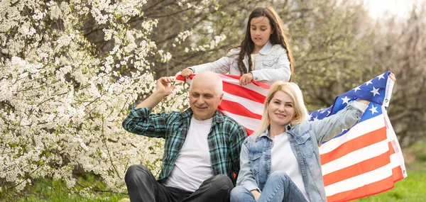 Portrait of happy family celebrating 4th July Independence Day holding silhouette usa national flag against park — 스톡 사진
