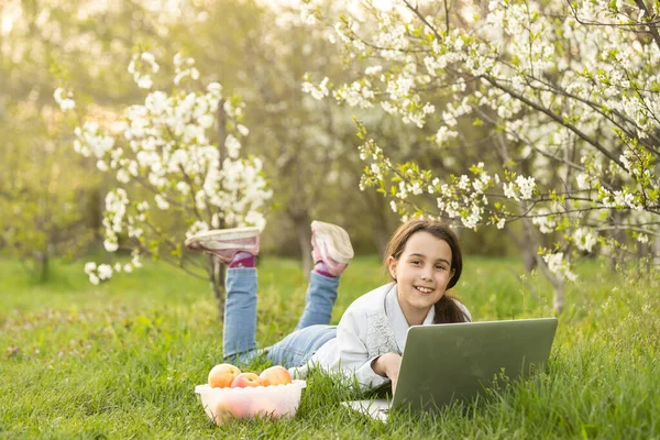 Smart little girl using her laptop in the garden. — Stock Photo, Image