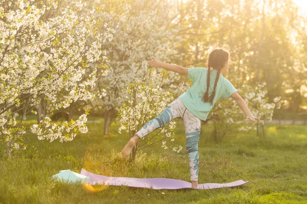 Tişörtlü küçük kız bahçede minderde yoga yapıyor. bir çocuk ve sağlıklı bir yaşam tarzı