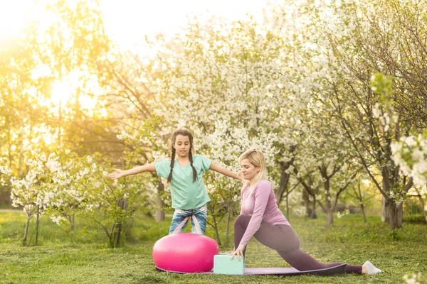 İki genç kadın ve bahçelerinde yoga yapan küçük bir kız.