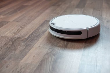 Kaplamalı ahşap zeminde beyaz bir elektrikli süpürge robotu. Oturma odasını temizleme fikri.