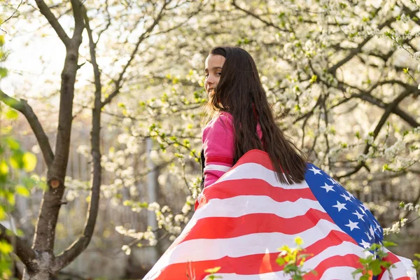 Gülümseyen ve Amerikan bayrağı sallayan sevimli küçük kız. Vatansever bayram. Mutlu çocuk, Amerikan bayrağı taşıyan şirin küçük kız çocuğu. ABD 4 Temmuz 'u kutluyor. Bağımsızlık Günü kavramı.