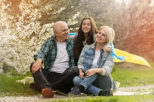 Familie mit großer Fahne der Ukraine in den Händen vor dem Hintergrund eines blühenden Baumes. Patriotische Erziehung. Stolz, Freiheit — Stockfoto