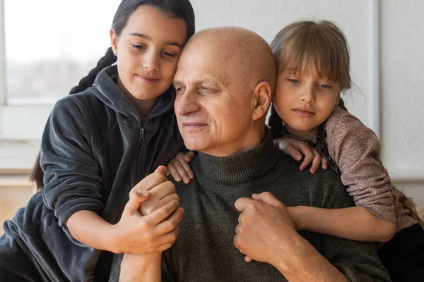 Grandfather and two granddaughters hugging on sofa at home — Stock Photo, Image