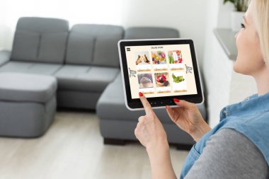 Mutfakta dijital tablet kullanan bir kadın çevrimiçi yiyecek alışverişi yapıyor, tablet ekranda yakın çekim yapıyor. Tablet kullanarak çevrimiçi satın alma kavramı.