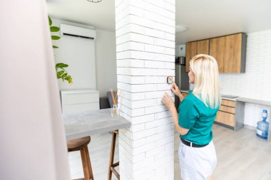 Bir kadın evin termostatına iliştirilmiş bir duvarın yukarı düğmesine basıyor ve sıcaklığı dijital ortamda gösteriyor. Elektrik faturası, ısıtma, soğutma, çevre dostu, tasarruf vesaire için bir konsept resim