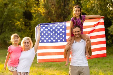 Amerikan bayrağı taşıyan ebeveynler ve çocuklar renkli bir uçurtmayla oynuyorlar. Anne, baba ve küçük kızları sisli bir günde 4 Temmuz 'u birlikte kutluyorlar. ABD 'nin Bağımsızlık Günü konsepti.