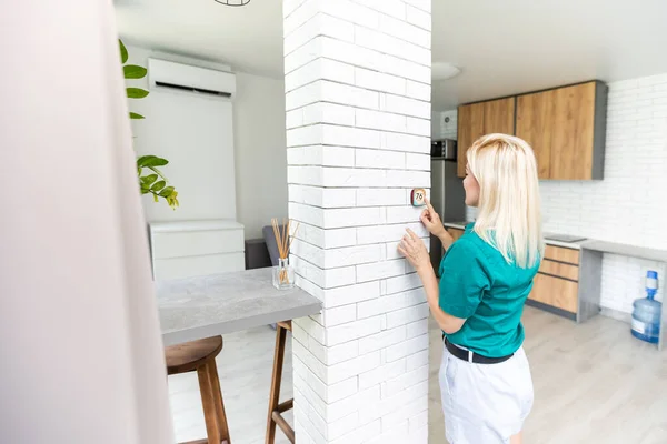 Una mujer está presionando el botón hacia arriba de un termostato de la casa adjunta a la pared con pantalla digital que muestra la temperatura. Una imagen conceptual para la factura de electricidad, calefacción, refrigeración, respetuoso del medio ambiente, ahorro, etc. — Foto de Stock