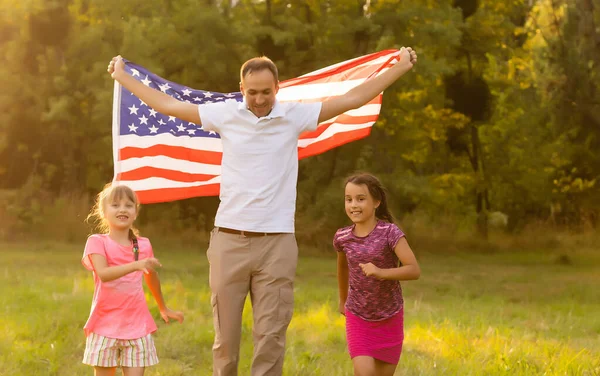 Happy family with the flag of america USA at sunset outdoors — Stock Photo, Image
