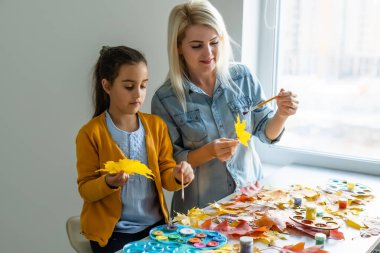 Anne ve kızı sonbahar yapraklarını boyarlar.