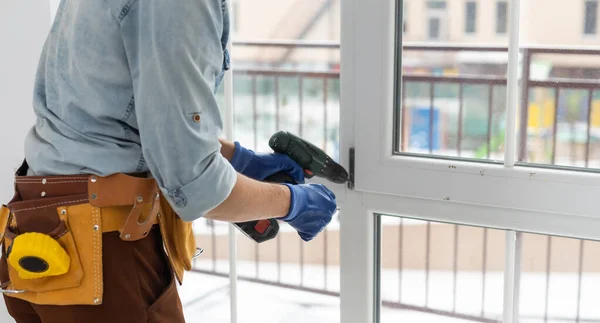 Um homem endireita uma janela ou porta de plástico com uma chave de fenda. — Fotografia de Stock