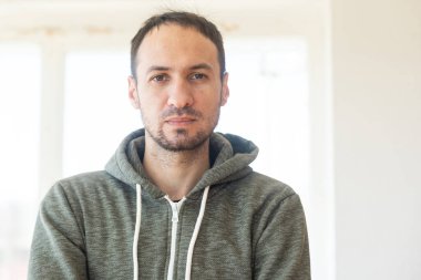 Sakallı, orta yaşlı bir adam kameraya bakıyor. Kafasında ve omuzlarında ciddi bir ifade var.