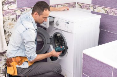 Çalışan tesisatçı çamaşırhanedeki çamaşır makinesini tamir ediyor.
