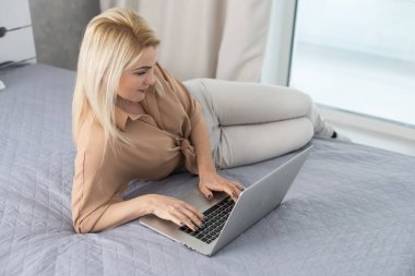 Kanepede oturup dizüstü bilgisayar kullanan mutlu bir kadın. Karantina sırasında uzaktan çalışma veya öğrenim kavramı