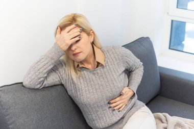 Ağrı ile yatağın üstüne oturan genç kadın