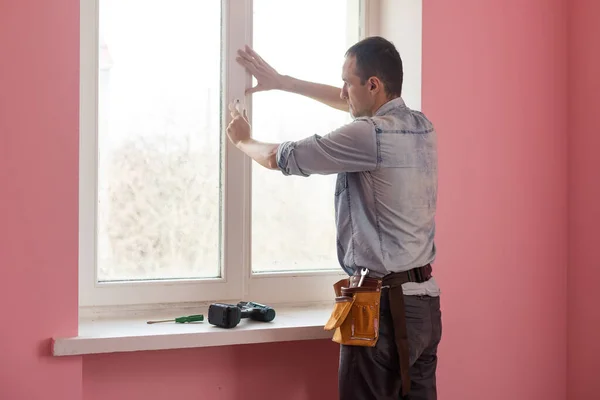 Handyman använder en sladdlös skruvmejsel för att installera ett fönsterhandtag. Kvalificerade arbetare tjänster, hem reparation och renovering. — Stockfoto