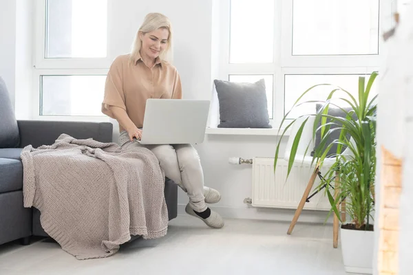 Mosolygó boldog nő ül a kanapén és laptopot használ. A távmunka vagy a karantén alatti tanulás fogalma — Stock Fotó