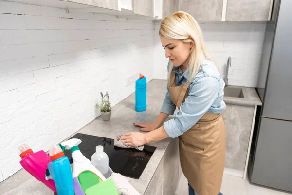 İnsanlar, ev işleri ve ev işleri konsepti. Evde mutfağı süngerle temizleyen bir şişe sprey ile sarışın orta yaşlı kadın..