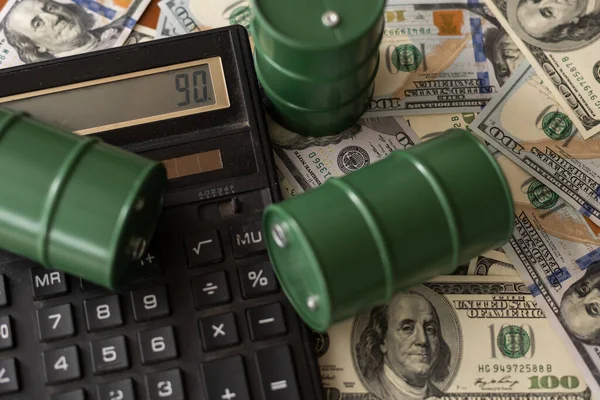 Barris com petróleo, uma calculadora contra o fundo de notas de dólar. negócios petrolíferos. — Fotografia de Stock
